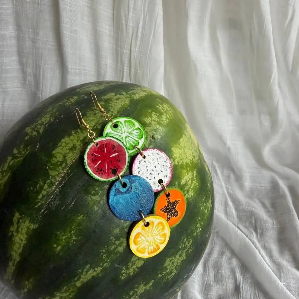 Hand-painted fruit stack earrings resting on a watermelon