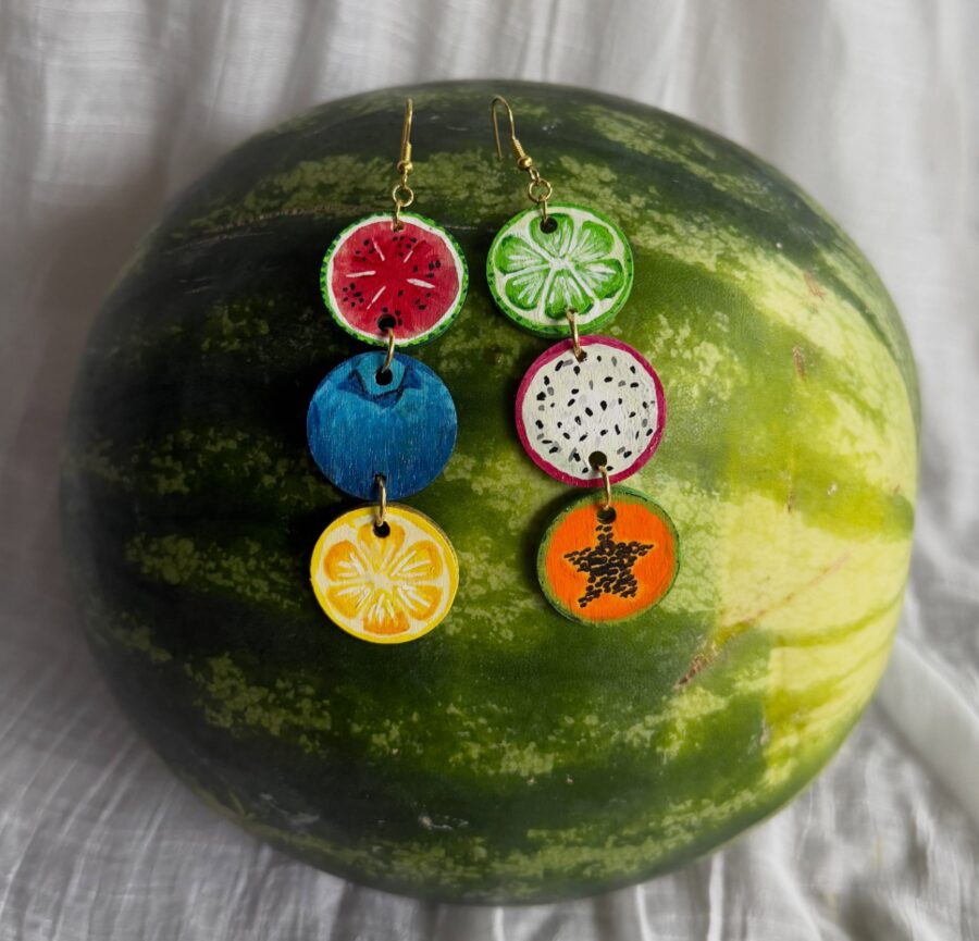 Hand-painted fruit slice earrings resting on a watermelon